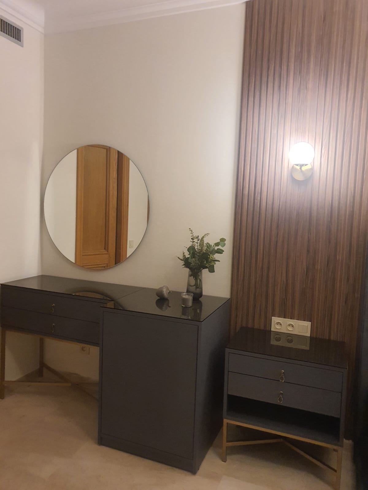 Coiffeuse noire devant un panneau mural en bois cannelé avec miroir rond