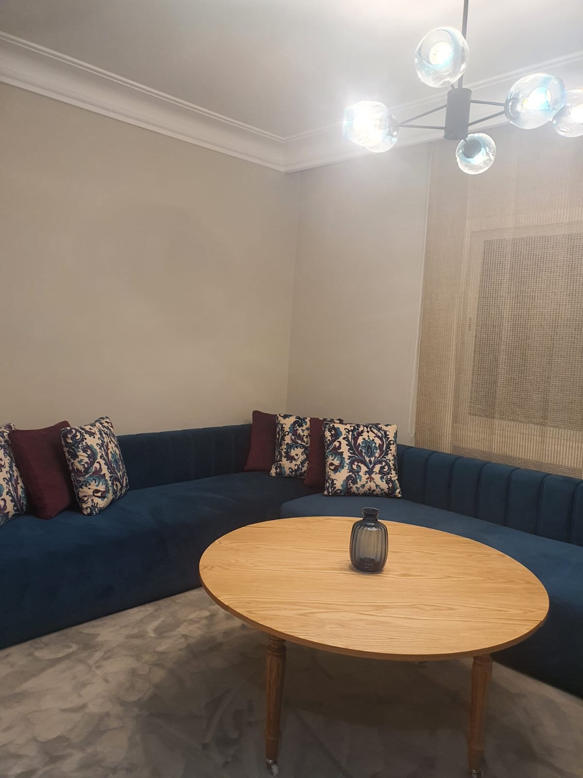 Salon avec banquette d'angle en velours bleu et table basse ronde en bois