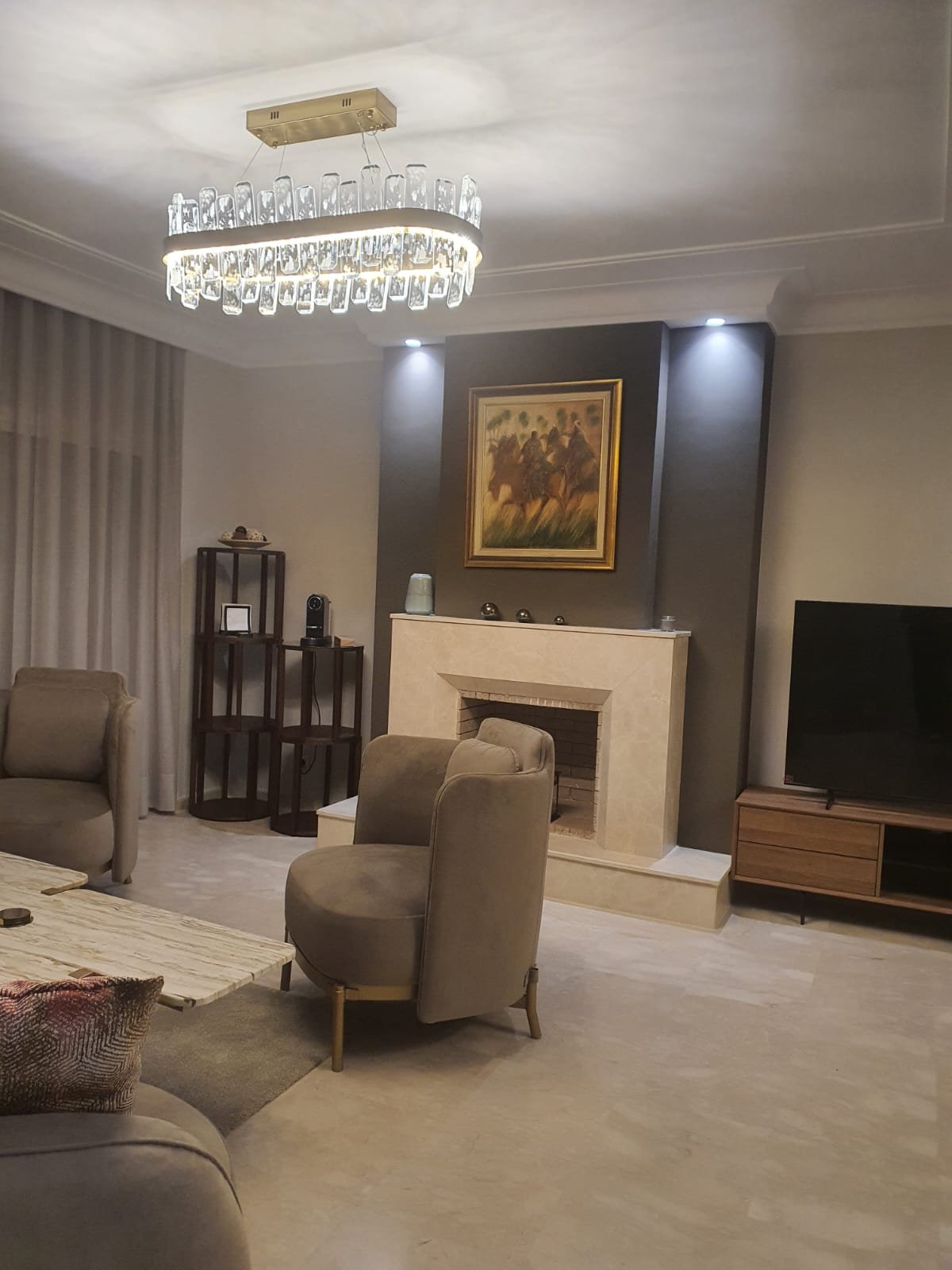 Séjour avec cheminée en pierre, lustre en cristal et fauteuils beiges