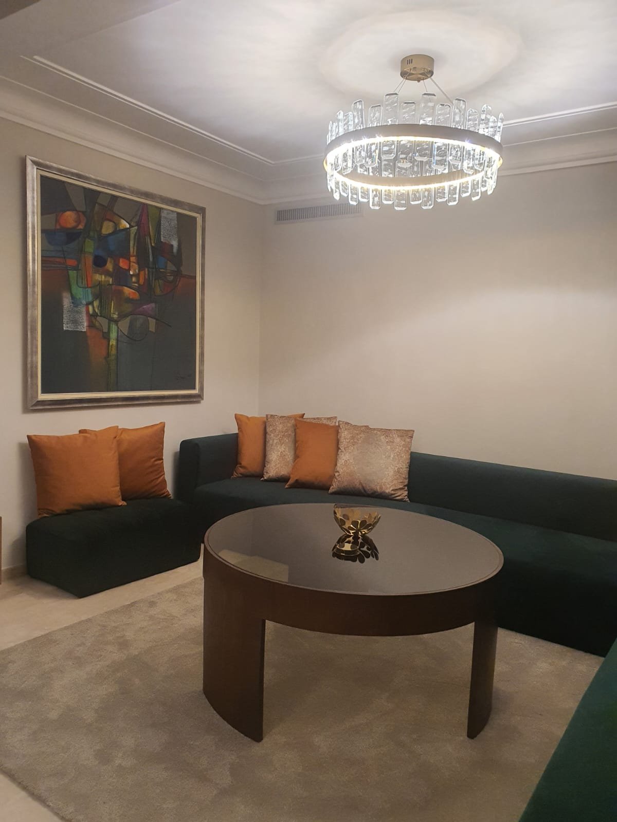 Salon avec banquette en velours vert, coussins orange et table basse ronde